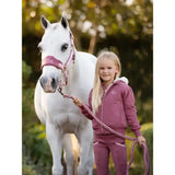 A young girl wearing the lemieux sherpa lined lily hoodie orchid in mauve stands beside a white horse holding its lead rope