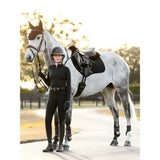 A woman in black equestrian gear stands next to a dapple gray horse with a lemieux suede close contact square black saddle pad