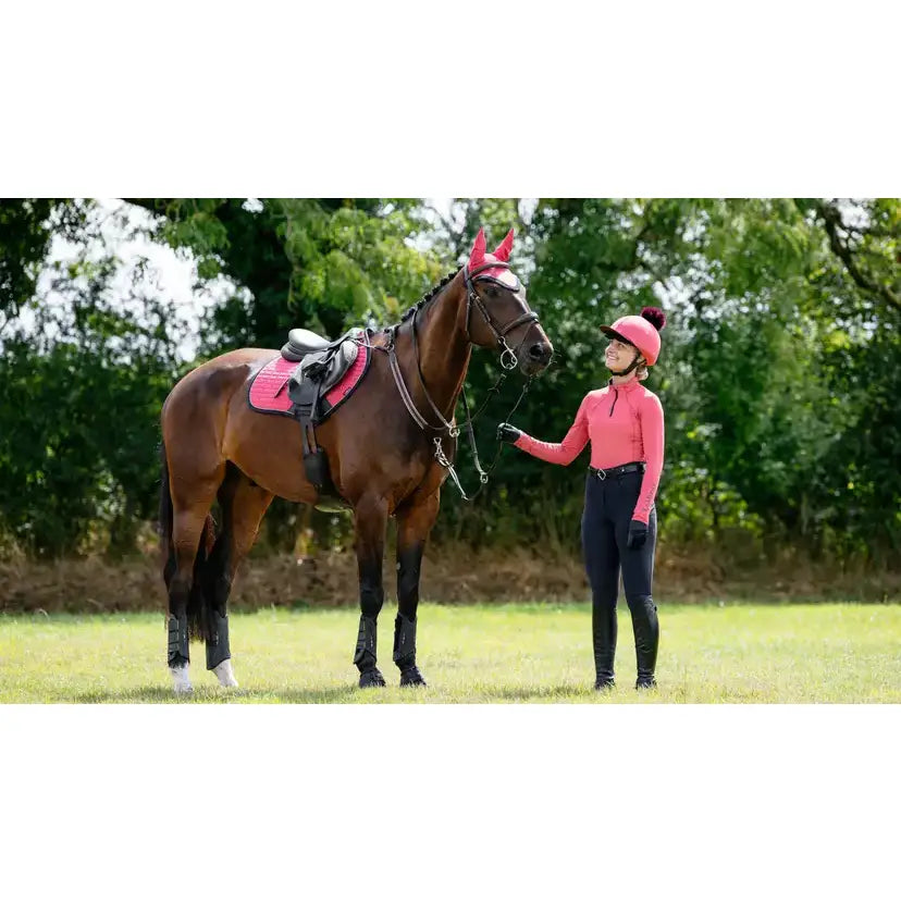 A brown horse wearing a lemieux suede close contact square cranberry saddle pad and matching ear covers in a grassy field