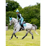 A rider in light blue gear sits on a dapple grey horse wearing matching turquoise lemieux suede close contact square lagoon pads