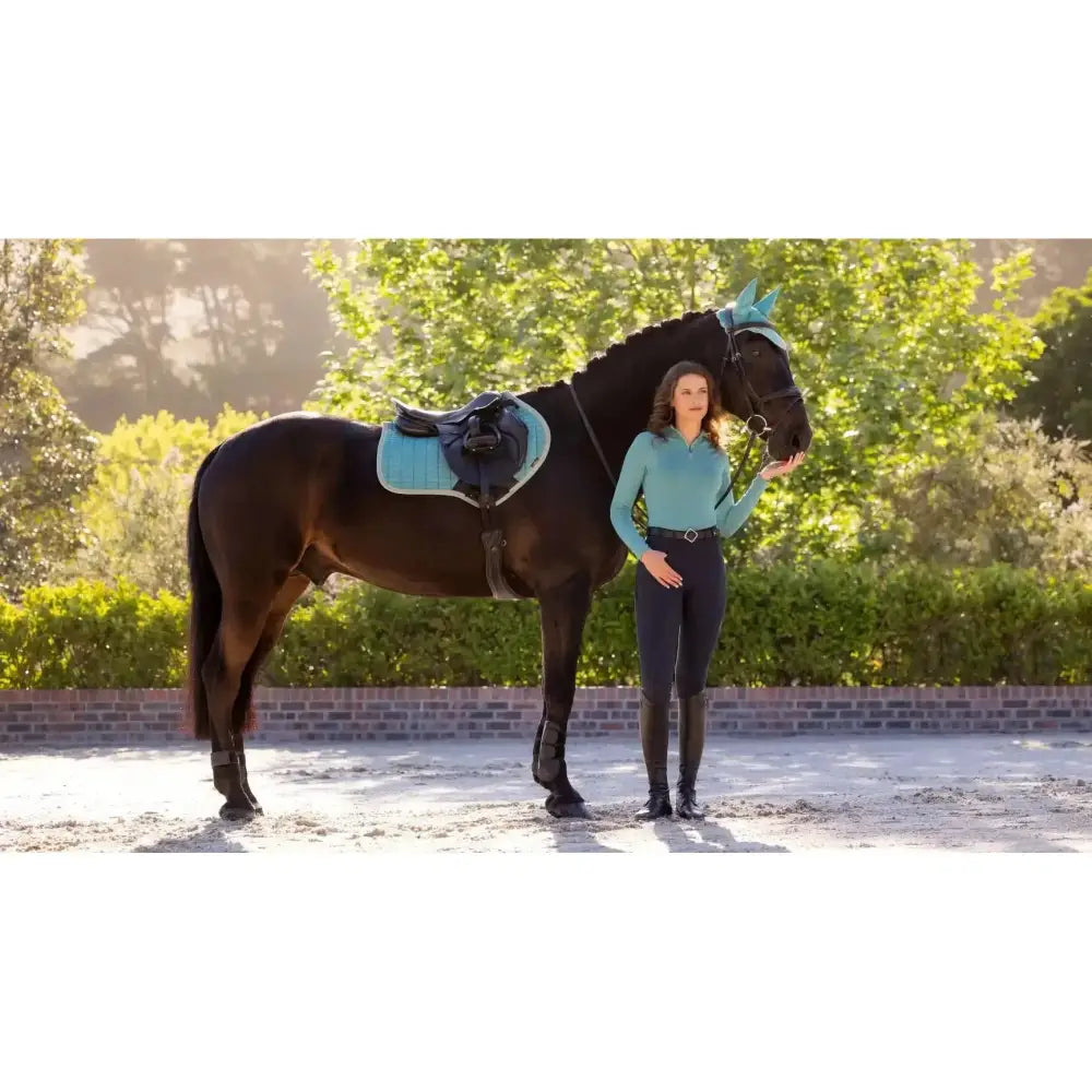 A sleek black horse with a turquoise lemieux suede close contact square lagoon saddle pad and bridle standing calmly