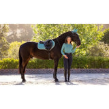 A sleek black horse with a turquoise lemieux suede close contact square lagoon saddle pad and bridle standing calmly
