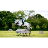 A white horse wearing lemieux suede close contact square lagoon teal protective gear mid-jump with matching rider