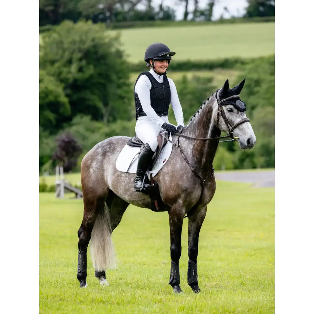 A dapple gray horse wearing a lemieux suede close contact square white suede saddle pad with black leg wraps