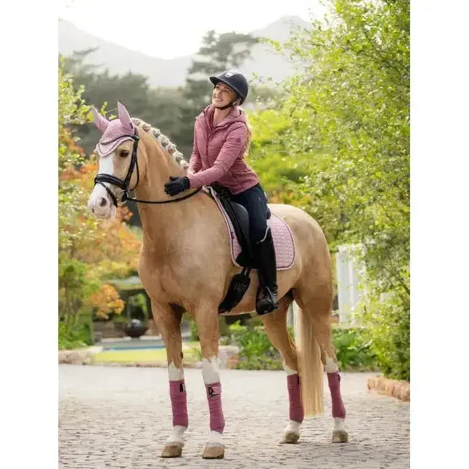 A light brown horse wearing a lemieux suede dressage square blossom with pink bridle and leg wraps outdoors