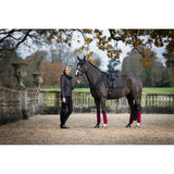 Dark horse with pink leg wraps beside person in black coat and Lemieux Suede Dressage Square