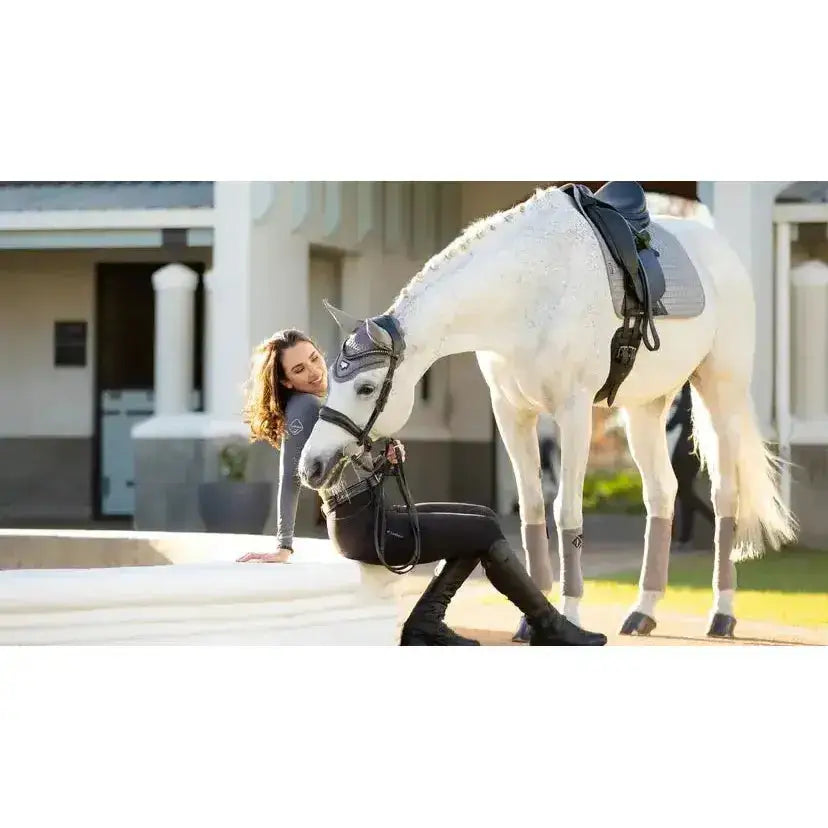 A white horse wearing a lemieux suede dressage square grey with soft suede binding and black leather tack