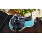 A sleek black lemieux suede gp square saddle on a quilted turquoise square lagoon saddle pad for equestrian use