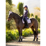 A young rider on a dark brown horse wearing a lemieux suede gp square lilac saddle pad and white protective leg wraps