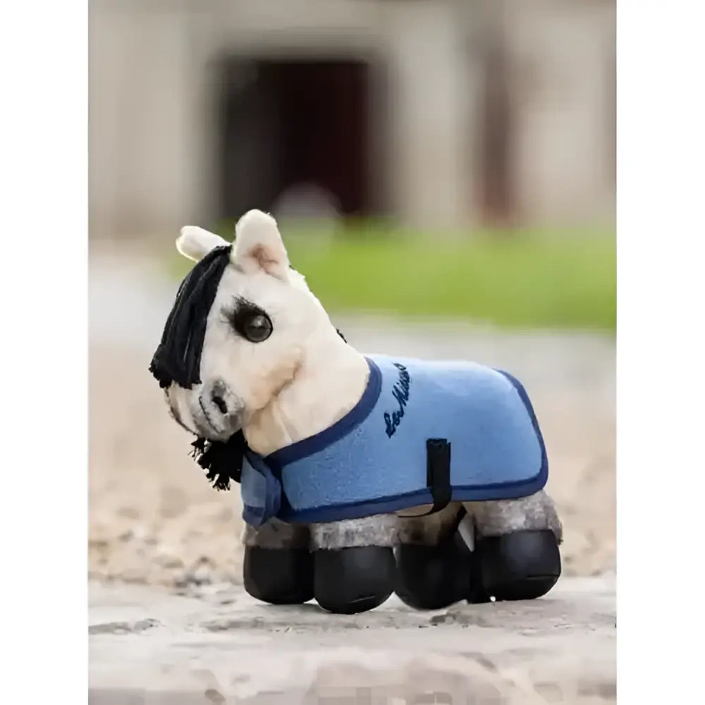 A plush white horse figurine wearing a light blue riding blanket with black trim and lemieux tiny pony dream branding