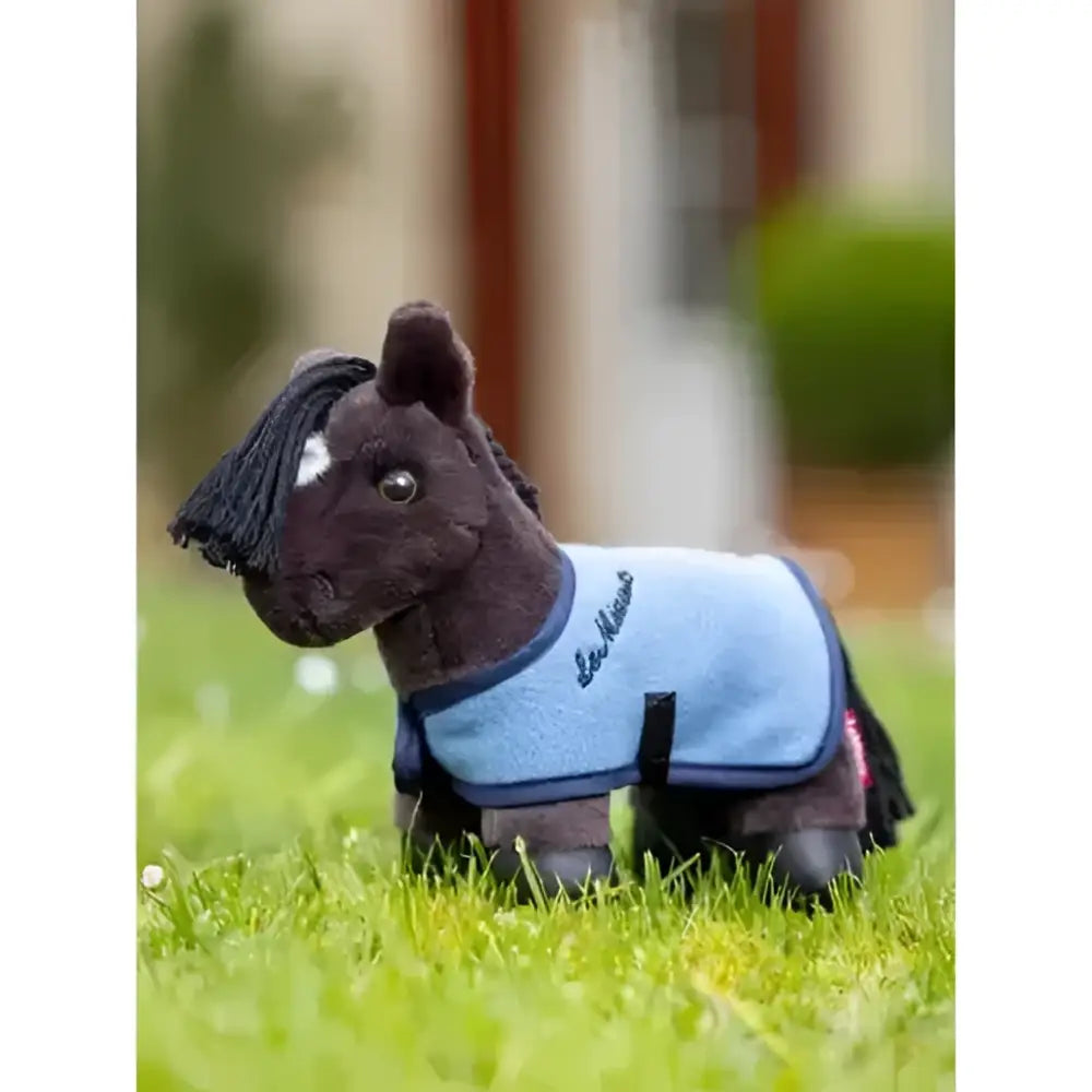 A plush black horse toy wearing a light blue lemieux tiny pony freya protective blanket with dark blue trim and logo