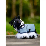 A plush black and white cow patterned toy pony wearing a light blue fleece blanket with navy trim lemieux tiny pony razzle
