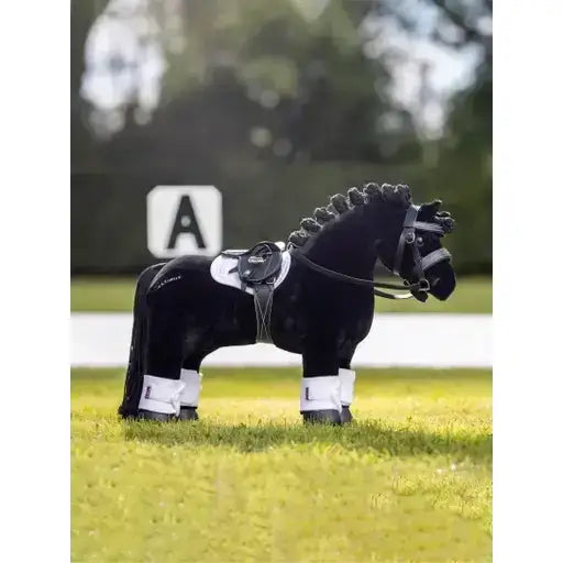 Black lemieux toy pony plush with white saddle and pony bridle black standing on green grass