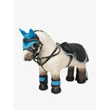 A plush white lemieux toy pony with blue knitted ear covers and navy pony exercise sheet leg wraps and saddle