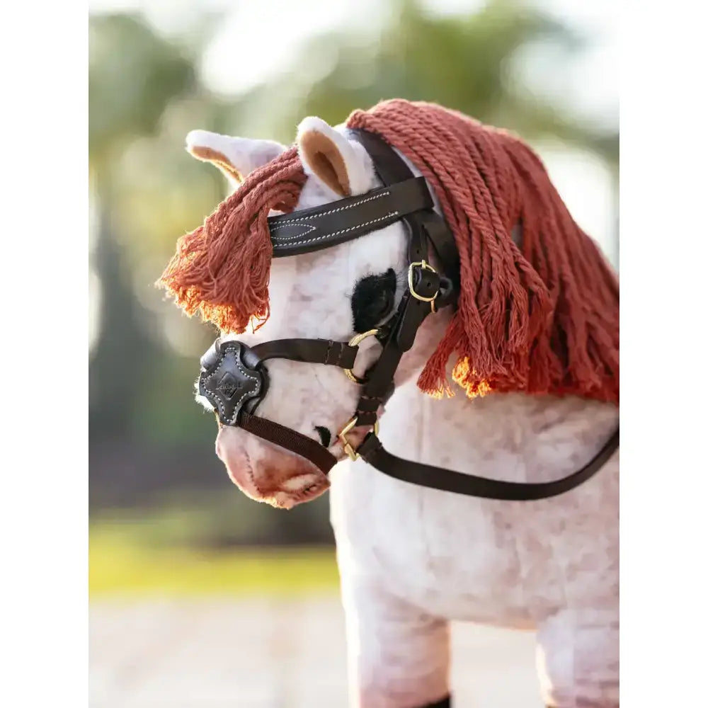 A plush white lemieux toy pony with rust-colored braided mane and grackle bridle brown leather harness with gold hardware