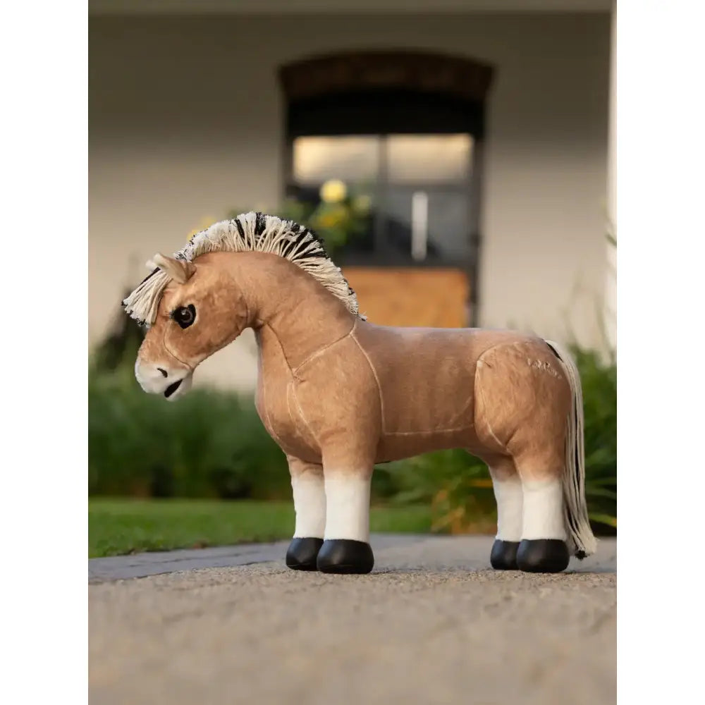 A plush tan lemieux toy pony oskar with white socks and black hooves stands on a paved surface