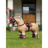 A plush tan lemieux toy pony wearing a black and red saddle pad cranberry with matching bridle and leg wraps