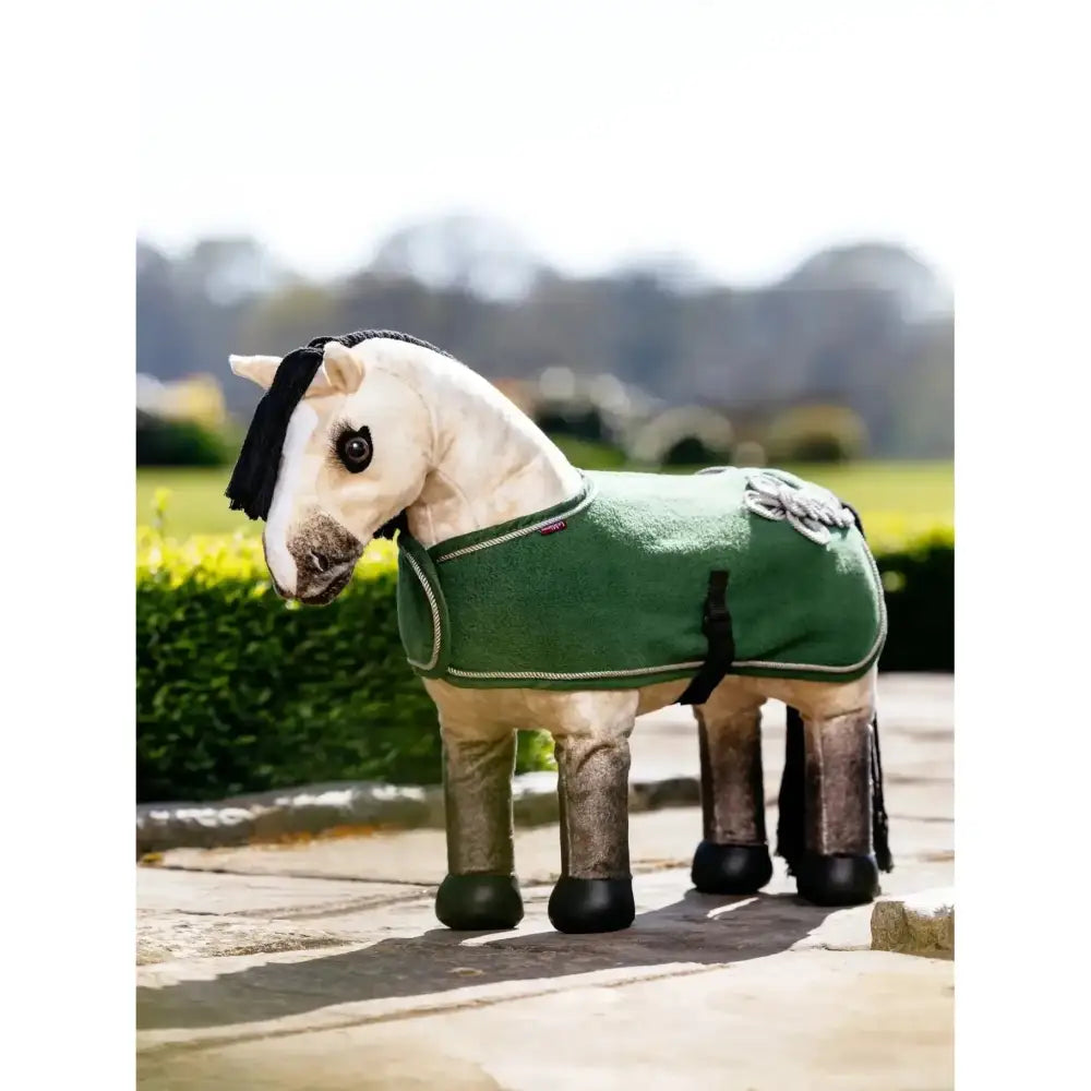 A plush white lemieux toy pony wearing a green felt toy pony rug with black trim and silver embroidery