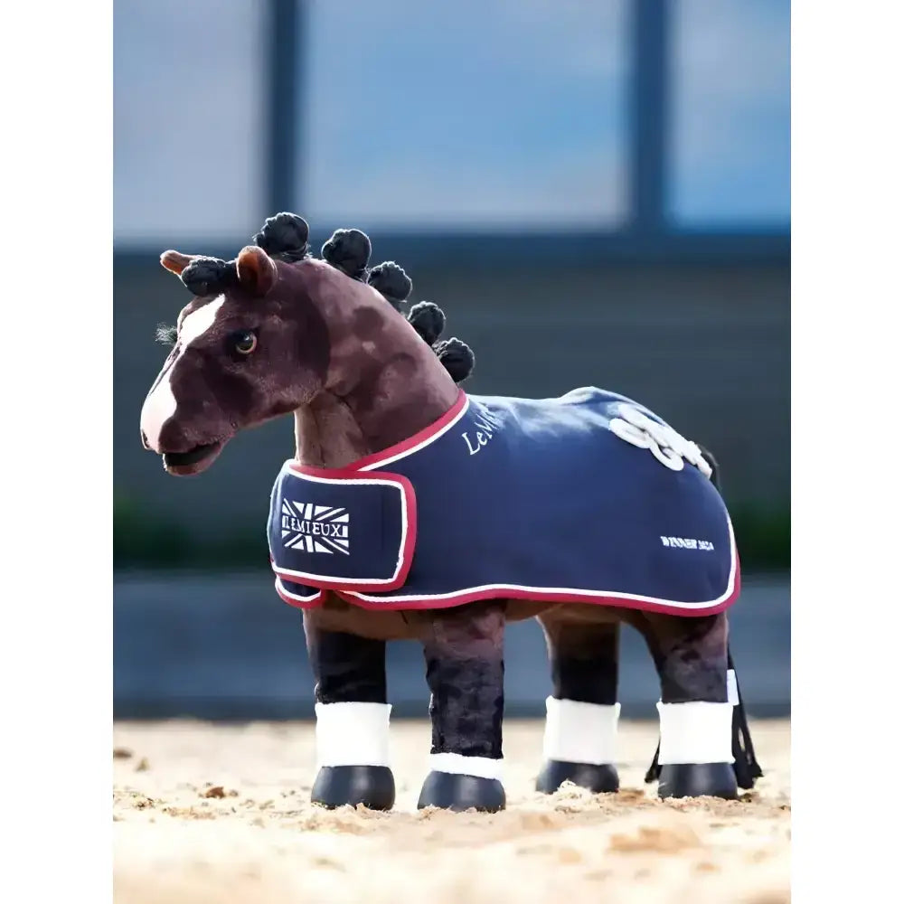 A plush brown lemieux toy pony wearing a navy blue pony winners rug with red trim and a union jack patch on the chest