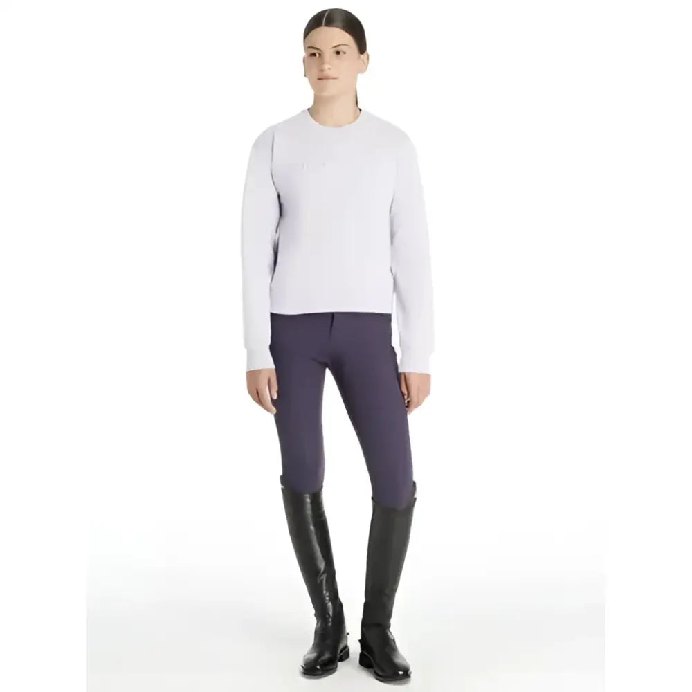 A woman wearing a lemieux young rider carmen crew sweat lilac light gray sweater with dark purple riding pants and boots