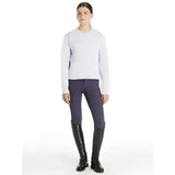 A woman wearing a lemieux young rider carmen crew sweat lilac light gray sweater with dark purple riding pants and boots