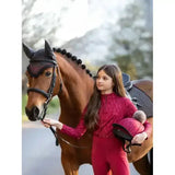 The girl wears a vibrant red long-sleeved lace lemieux young rider casey base layer ember with matching leggings