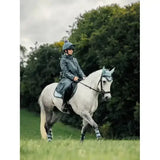 A white horse wearing a dark green helmet and leg wraps with lemieux young rider elements coat petrol gear