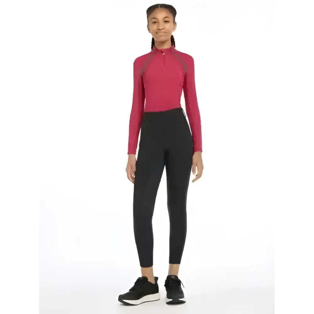 A woman wearing lemieux young rider ella winter breggings black with a pink long-sleeved athletic top and black panels
