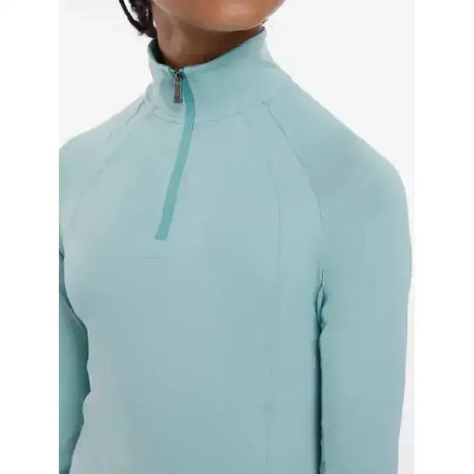 A light blue lemieux young rider hope lightweight base layer with long sleeves and a high collar zipper
