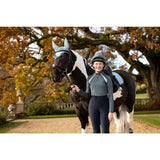 A black and white pinto horse wearing a silver mesh ear cover with lemieux young rider mia mesh base layer petrol