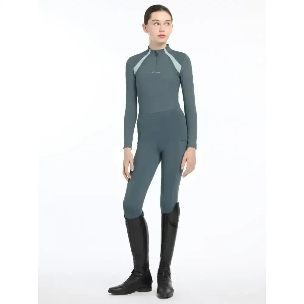 A sleek dark gray lemieux young rider mia mesh base layer with light gray shoulders and subtle logo on the chest