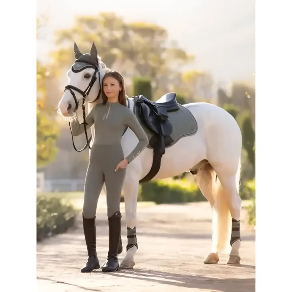 A woman in grey sleek lemieux young rider orla pull ons rosemary leggings stands beside a white horse