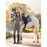A woman in grey sleek lemieux young rider orla pull ons rosemary leggings stands beside a white horse