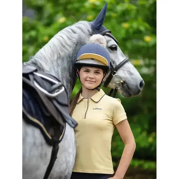A young girl wearing a lemieux young rider polo shirt mimosa and navy blue gold equestrian helmet