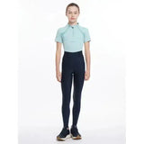 A woman wears lemieux young rider remi breggings navy with black riding pants and a light blue short sleeved polo shirt
