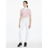 A woman wearing a pink equestrian top and lemieux young rider remi breggings white riding pants