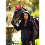 A young woman wearing a lemieux young rider tammy teddy fleece navy stands beside a horse with red ear protection
