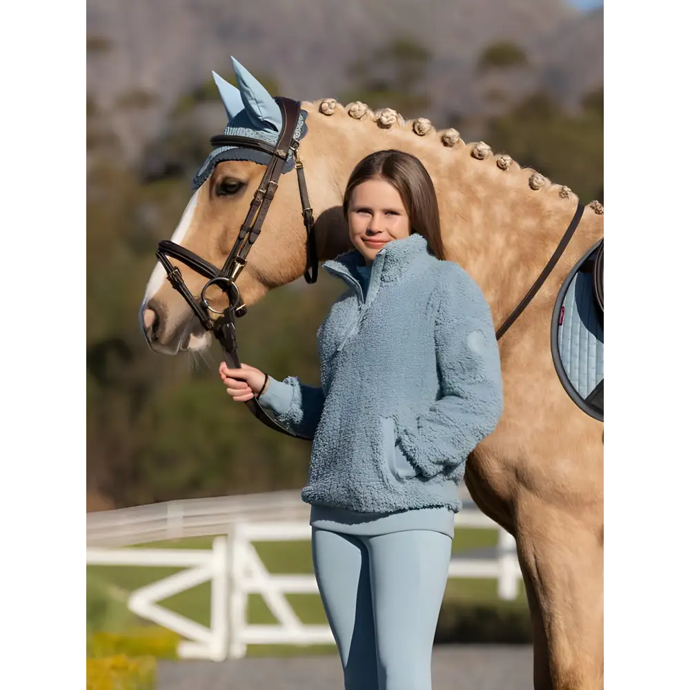 Palomino horse with braided mane beside person in blue wearing Tia Teddy fleece