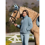 Palomino horse with braided mane beside person in blue wearing Tia Teddy fleece