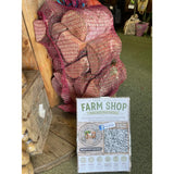 A red mesh bag of heart-shaped potatoes sits beside a wooden crate and farm shop sign near locally cut hardwood logs