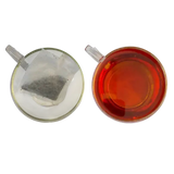 Clear glass teacup with amber miles tea decaffeinated teabags and unbrewed tea bag from west country