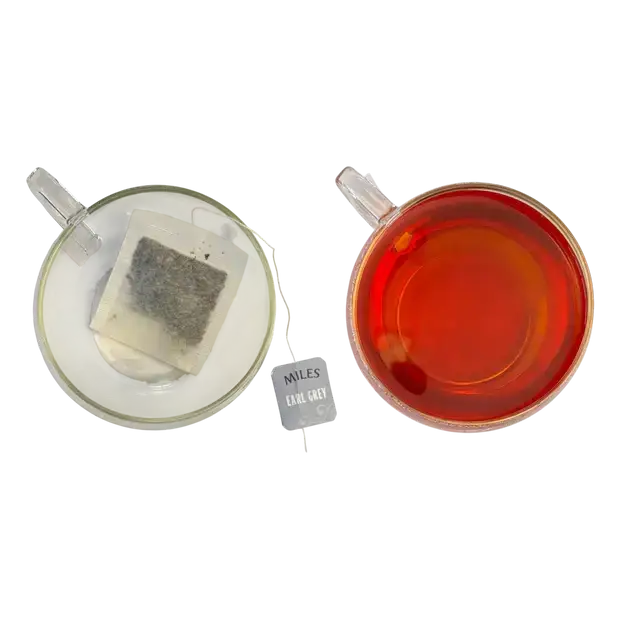 A clear glass teacup filled with amber earl grey tea and a miles earl grey loose-leaf tea bag from grey envelope teabags