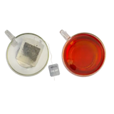 A clear glass teacup filled with amber earl grey tea and a miles earl grey loose-leaf tea bag from grey envelope teabags