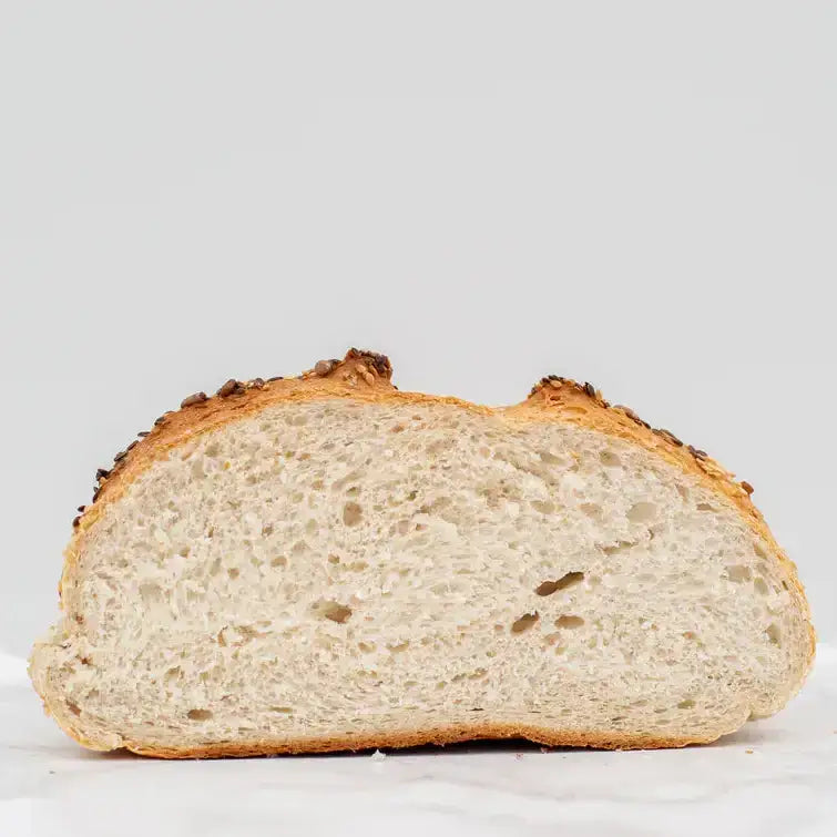 A golden-brown crusty mixed seed cob with a soft airy interior and seeds on top in a round loaf shape