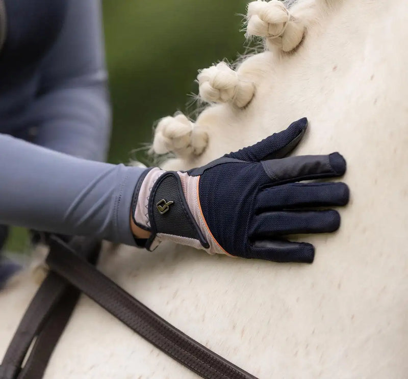 Navy blue equestrian glove with a pink and black wrist strap, featuring a small metallic logo on the back of the hand.