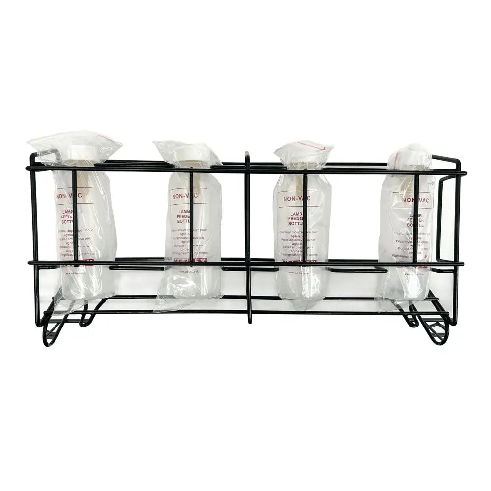 Black metal rack holding four clear plastic lamb feeder bottles sealed in bags with white caps nettex agri non-vac system
