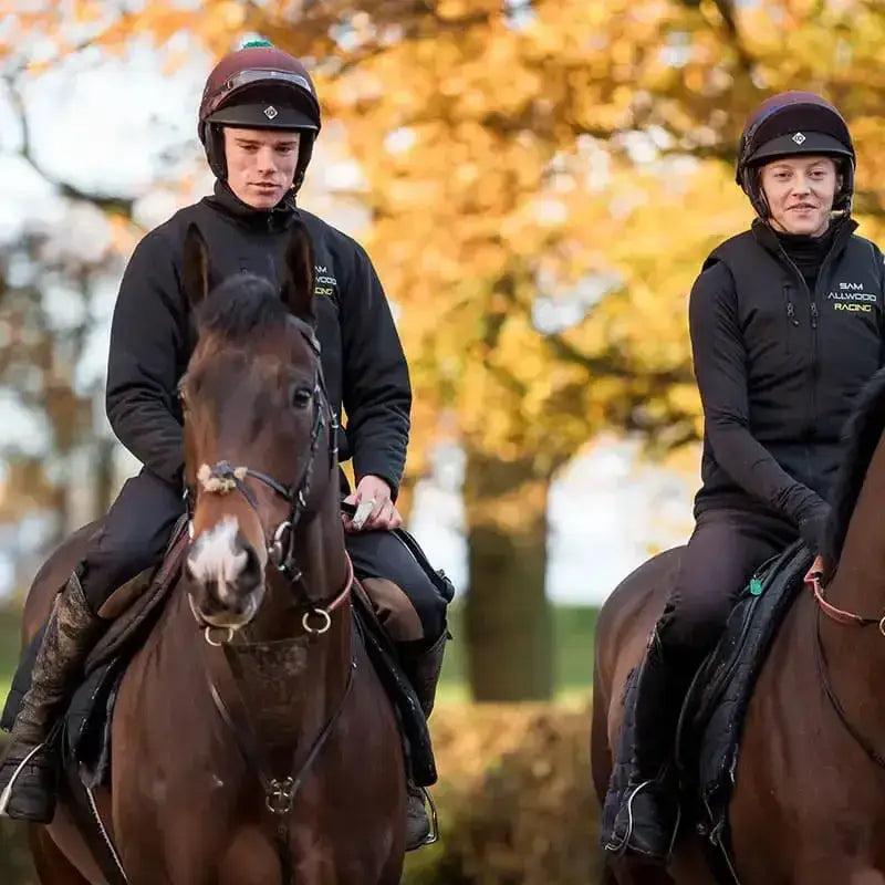 Two riders wearing black charles owen race ii riding hats on brown horses with white markings in autumn trees