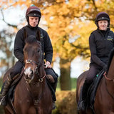 Two riders wearing black charles owen race ii riding hats on brown horses with white markings in autumn trees