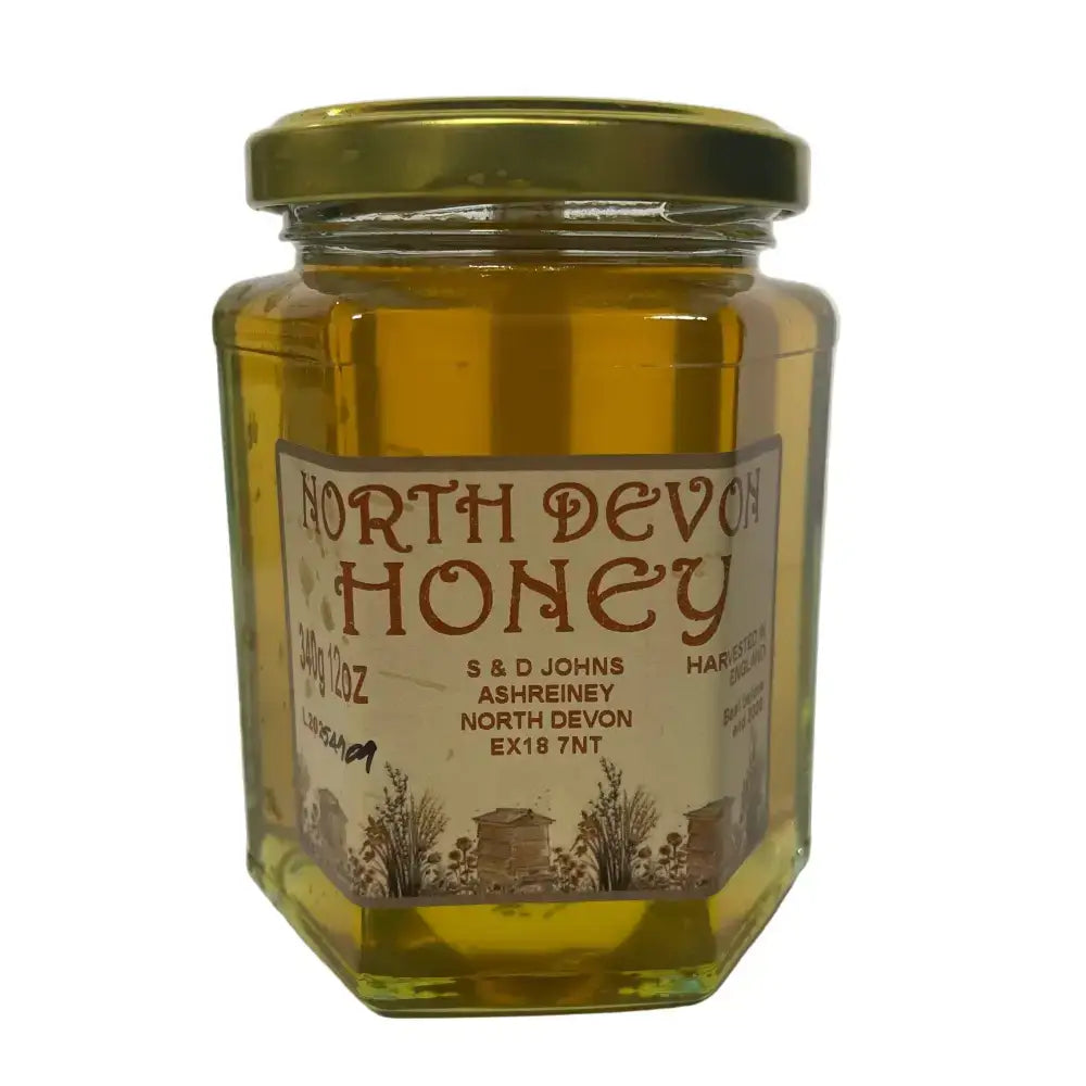 A hexagonal glass jar of golden raw spring blossom north devon honey sealed with a gold metal lid and s & d johns label