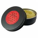 Black tin container with red label holding pale yellow cream bar made from north devon honey beeswax